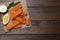 Fresh breaded fish fingers, sauce and lemon served on wooden table, top view. Space for text