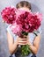 Fresh bright pink peonies on hands of faceless young woman in grey T-shirt on grey close up. Vertical orientation