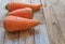 Fresh carrots are on the table: two of them are short, one slightly longer