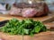 Fresh chopped greens in the foreground and a piece of meat blurred in the background.