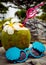 A fresh coconut with a red patterned straw and a fragrant plumeria flower stands on a stone, next to it there are