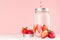 Fresh cold milkshake in hipster jar with cut ripe berries, striped straw, silver lid in elegance pink kitchen interior, closeup.