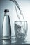 Fresh and cold, pure Water is poured into a glass with bottle. Purified water in a glass on a gray background. Motion freeze