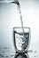 Fresh and cold, pure Water is poured into a glass. Purified water in a glass on a gray background. Motion freeze splash of crystal