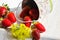 Fresh colorful strawberries spilled from bucket on garden table outdoors, yellow flowers, bright sunlight