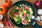 Fresh cooked scrambled eggs in pan with sausage and herbs. Bread, fork, vegetables on wooden board, top view.