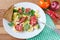 Fresh cooked scrambled eggs with sausage and herbs in white plate.Bread, napkin, fork, vegetables on wooden board.