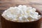 Fresh cottage cheese grain in a wooden bowl. Curd in granules with cream. Wooden rustic background. Copy space.