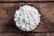 Fresh cottage cheese grain in a wooden bowl. Curd in granules with cream. Wooden rustic background. Copy space.