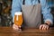 Fresh craft beer. Man in apron puts on wooden table glass of light ale with foam