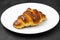Fresh croissant with a brown crust on a white plate on a black table.