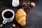 Fresh croissant with a mug of i black coffee and coffee beans