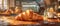 Fresh croissant on wooden table in a cozy, sunlit bakery with pastries and coffee machine in the background.