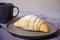 Fresh croissants buns on the gray plate and cup of coffee nearby