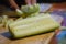Fresh cucumber on a wooden board with a female chopping another piece in the background