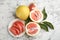 Fresh cut and whole pomelo fruits with leaves on white marble table, flat lay