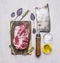 Fresh, delicious raw pork steak on a cutting board with butcher knife for meat, oil, salt herbs on wooden rustic background to