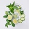 Fresh detox spring cocktail with mint, lime, ice, cucumber, straw as border on soft white wooden board, top view.