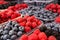 Fresh forest raspberries, blueberries and blackberries in plastic trays at market. Background.