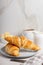 Fresh french croissants on plate and cup of coffee in the morning light. White cup of americano coffee.