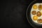 fresh fried eggs with onion rings in a frying pan on a black textured plaster background. top view. artistic dark moody photo with
