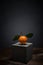 Fresh fruit on dark background on concrete stand. Bright orange tangerine with leaves with sharp thorns