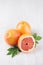 Fresh glossy whole grapefruits and round slice with green leaves on white wood plank with copy space, vertical.