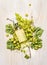 Fresh grapes on branch with leaves and bottle of white wine on white wooden background, top view