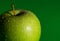 Fresh green apple partially seen with water drops on green background.