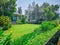 Fresh green grass smooth lawn as carpet on backyard with flowering tree and bush, greenery trees on background, good maintenance