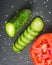 Fresh green sliced cucumber and tomato on a black stone background.