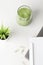 fresh green smoothie on desktop with laptop and flower on white background. Healthy snack in office. copy space.