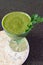 Fresh green smoothie in a wide glass on stem on the kitchen countertop - close up front top view