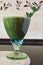 Fresh green smoothie in a wide glass on stem on the kitchen countertop - close up front top view