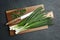 Fresh green spring onions, cutting board and knife on black table