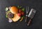 Fresh grilled and raw minced pepper beef burger on vintage chopping board with buns onion and tomatoes on black background. Salty