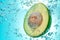Fresh half an avocado falls in water, bubbles around, in blue water. Trendy healthy diet.