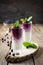 Fresh healthy blueberry smoothies in a glass with berries and mint leaves on a wooden stand.