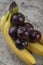 Fresh healthy plums with banana cluster on stone background