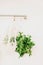 Fresh herbs, parsley, arugula hang in a white wicker reusable bag string bag in the snow-white minimalism kitchen.vertical content