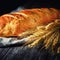 Fresh homemade loaf of bread with spikelets of rye on wooden background