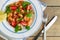 Fresh homemade salad of shrimp, arugula and tomato in a white plate on a wooden table, top view, flat lay, close up