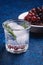 Fresh ice cold carbonated water in glass with rosemary leaf near to wooden bowl with grape berries, blue textured background