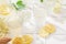 Fresh iced lemonade with lemons and elderberry flowers in a jar and glasses on white tile table with hard shadows