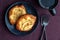 Fresh individual apple tarts on a black plate with forks, cup of hot tea, purple cloth background