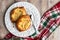 Fresh individual apple tarts on a white plate with fork, red, green, and white cloth napkin, wood background