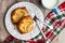 Fresh individual apple tarts on a white plate with forks, cup of milk, red, green, and white cloth napkin, wood background