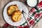 Fresh individual apple tarts on a white plate with forks, cup of milk, red, green, and white cloth napkin, wood background