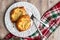 Fresh individual apple tarts on a white plate with forks, red, green, and white cloth napkin, wood background