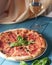 Fresh italian pizza with salami and black olives and other food on the background. Blue colored wooden table